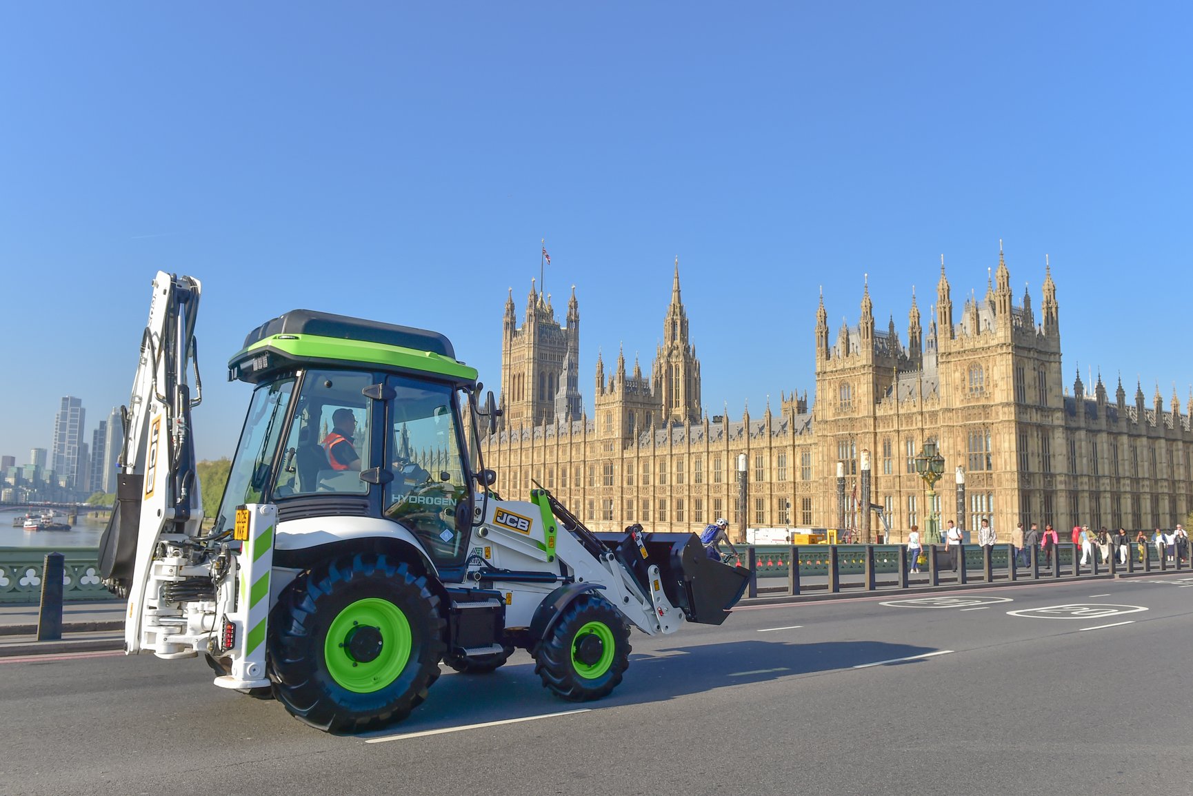 A hydrogen JCB digger drives over Westminster Bridge past Houses of Parliament