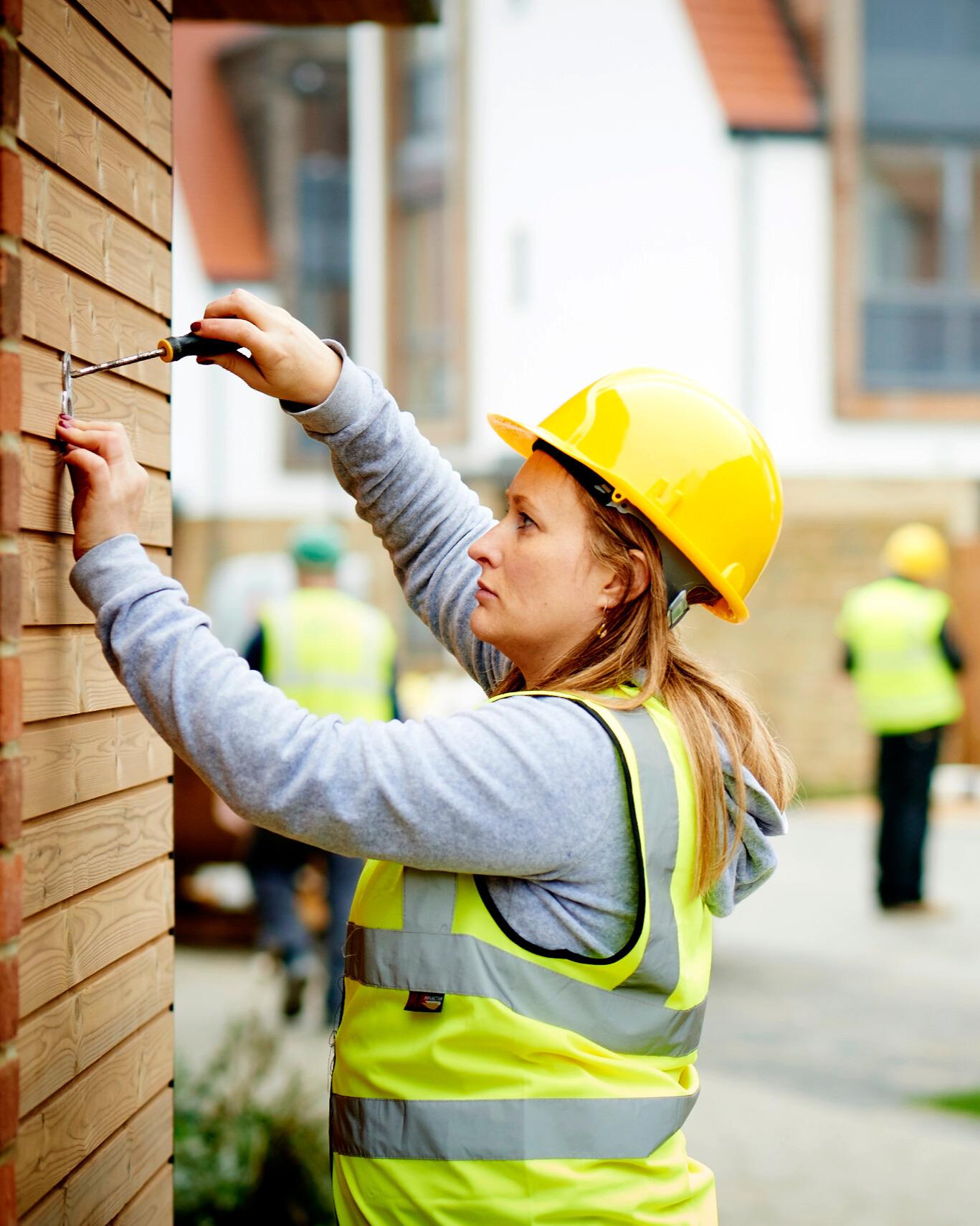 A female construction worker in a hard hat and high-vis vest using a screwdriver.